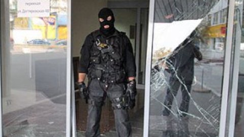 Сотрудники в форме спецназа с нашивками "милиция" и в масках охраняют вход.